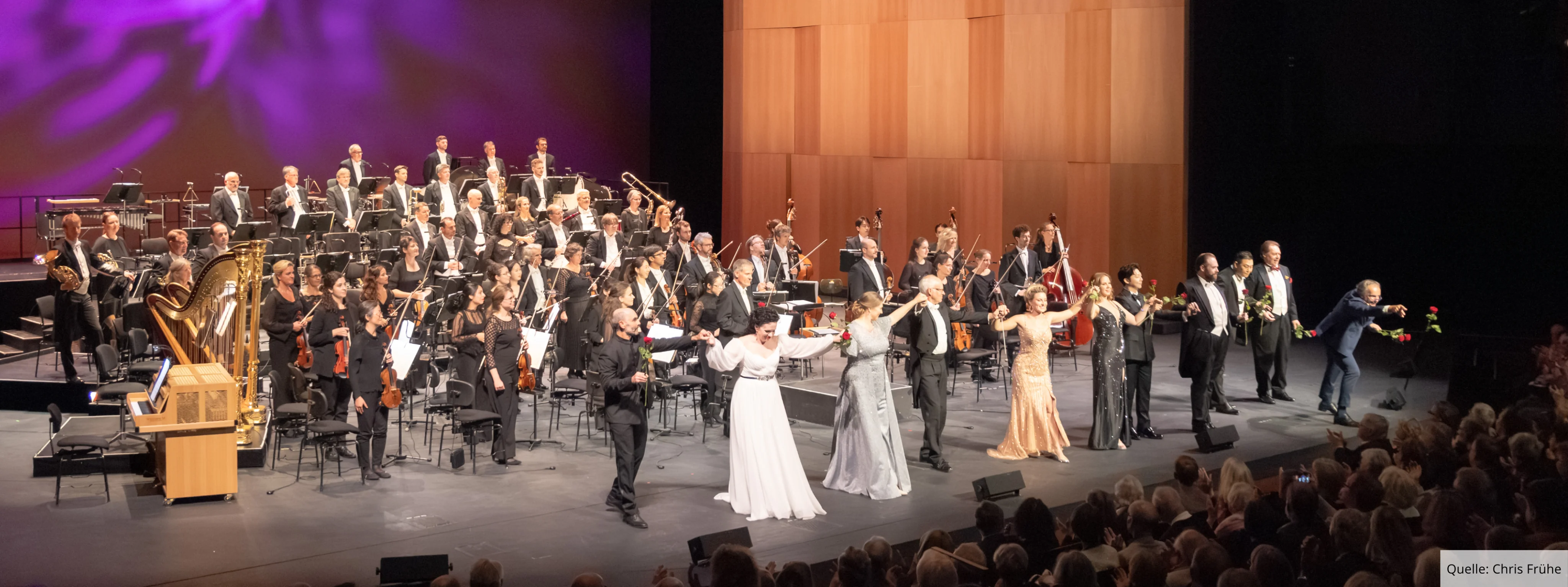 Ensemble und Orchester des Badischen Staatstheaters Karlsruhe beim Schlussapplaus auf der Bühne vor vollem Zuschauerraum